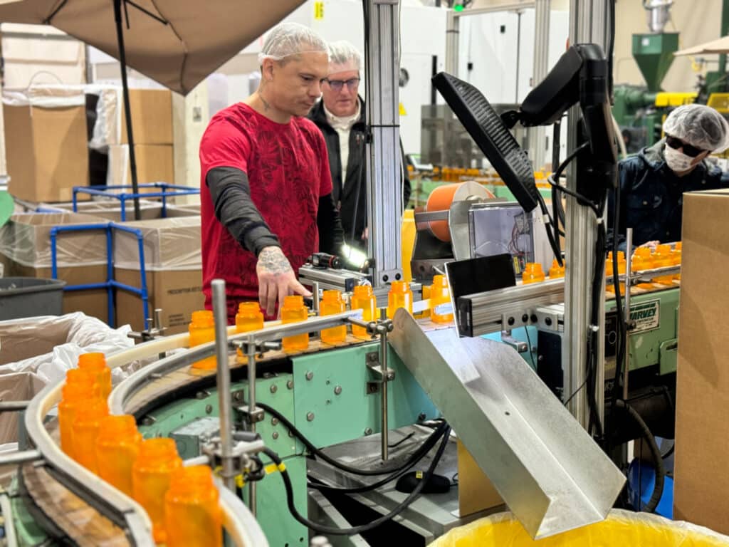 Two Alphapointe employees are standing near the production line. 